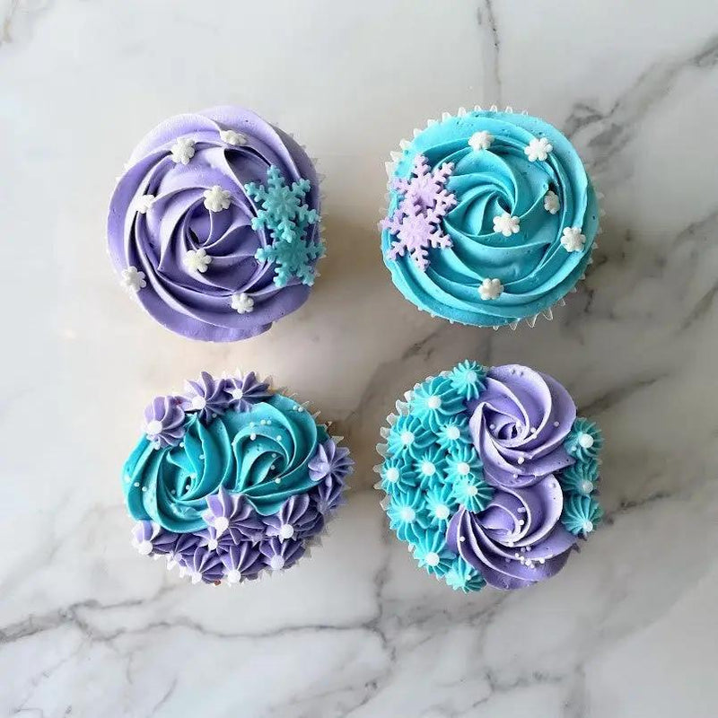 A set of four cupcakes with blue and purple buttercream frosting and a decorative snowflake.